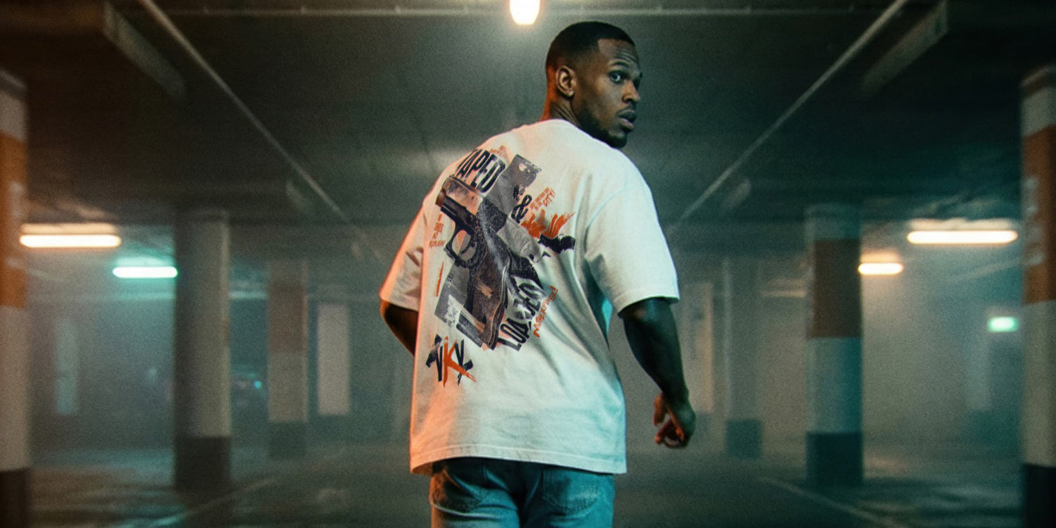 Mann dreht sich im Parkhaus um, trägt weißes Oversize T-Shirt 'TAPED & LOADED' mit großflächigem Backprint. Dramatisches Kunstlicht, cinematische Atmosphäre. Premium Cinematic Streetwear. Film Art Wear – Designed in Hamburg.