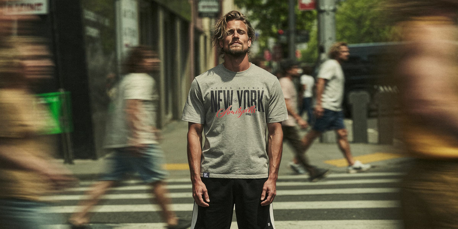 Organic T-Shirt 'AMITYVILLE NY' – Mann steht im urbanen Streetstyle-Look auf belebter Straße, Passanten im Bewegungsunschärfe-Effekt. Cinematischer Frontprint 'New York Amityville'. Premium Cinematic Streetwear. Film Art Wear – Designed in Hamburg.
