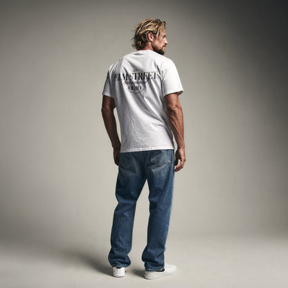 Organic T-Shirt 'ELM STREET' – Mann von hinten, weißes T-Shirt mit Backprint '1428 Elm Street Springwood Ohio'. Iconic Places Design. Premium Cinematic Streetwear. Film Art Wear – Designed in Hamburg.