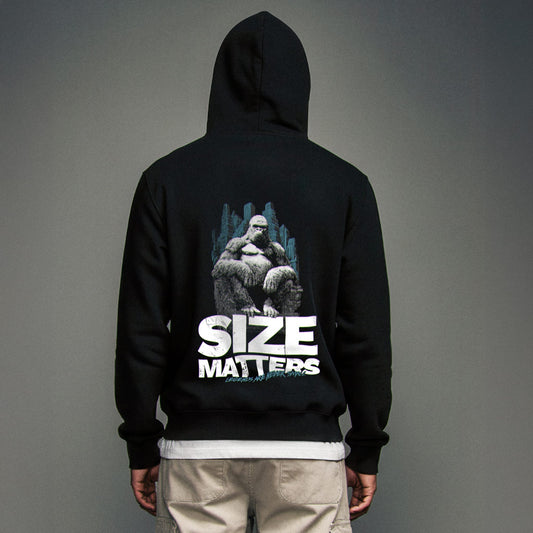Organic Hoodie 'SIZE MATTERS' – Mann von hinten, schwarzer Oversize Hoodie mit großflächigem Backprint 'Size Matters'. Heavy Oversize Fit. Premium Cinematic Streetwear. Film Art Wear – Designed in Hamburg.
